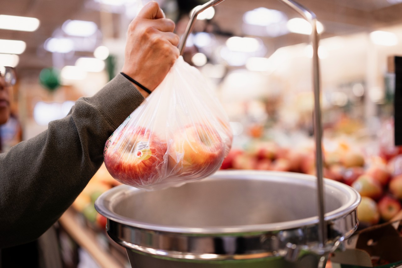 woman weighing plastic bag of apples in supermarket